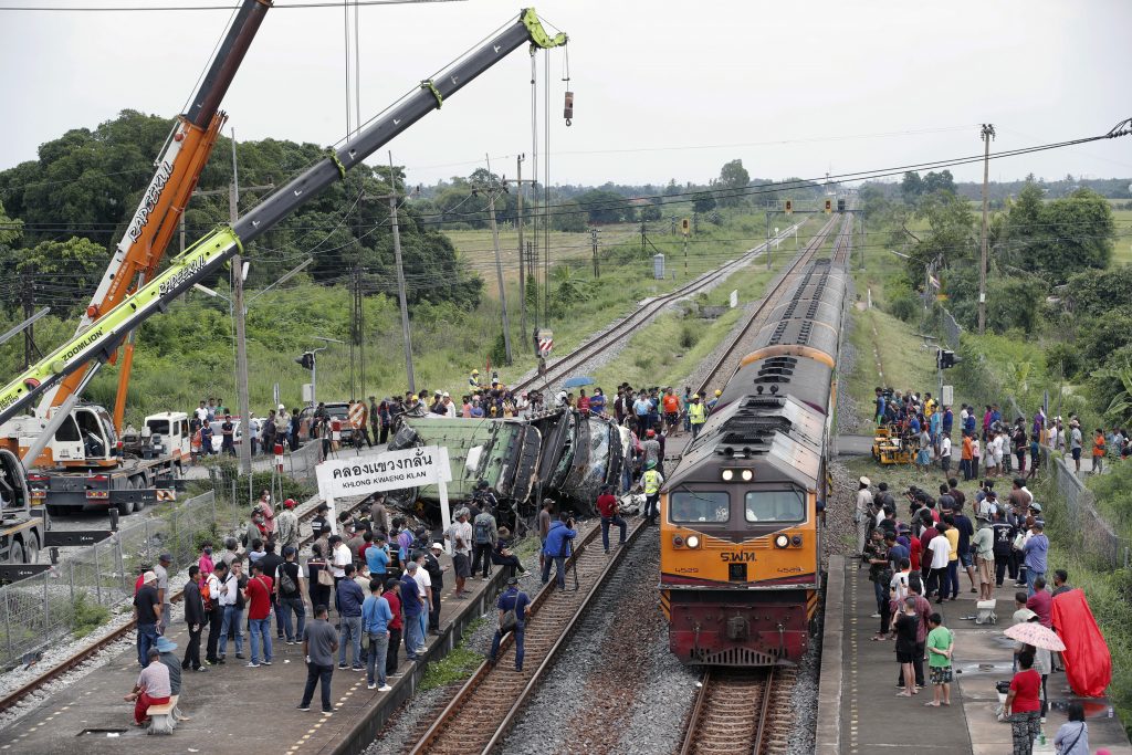 Een trein rijdt voorbij een wrak van een bus die in botsing is gekomen met een andere trein bij het station Khlong Kwaeng Klan railway in de provincie Chachoengsao in Thailand, foto: ANP