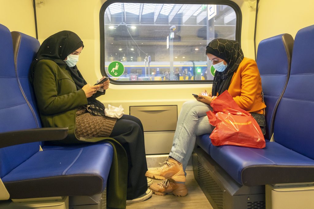 Twee jonge moslima's zitten in de trein op hun telefoon te kijken